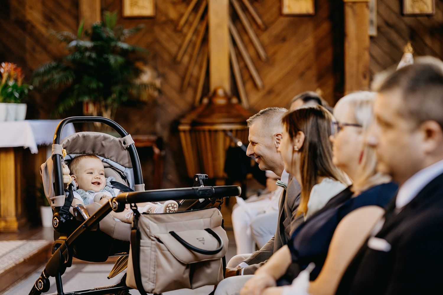 Happy baby in stroller surrounded by smiling family members during church service.
