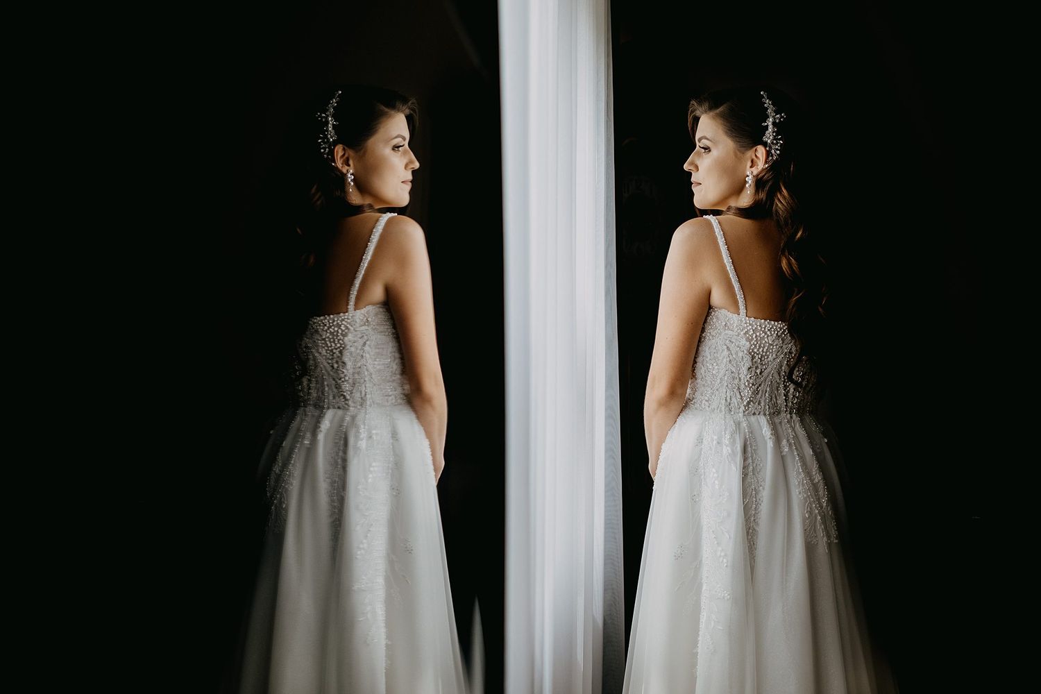 Elegant bride in lace wedding gown reflected in mirror by bright window.
