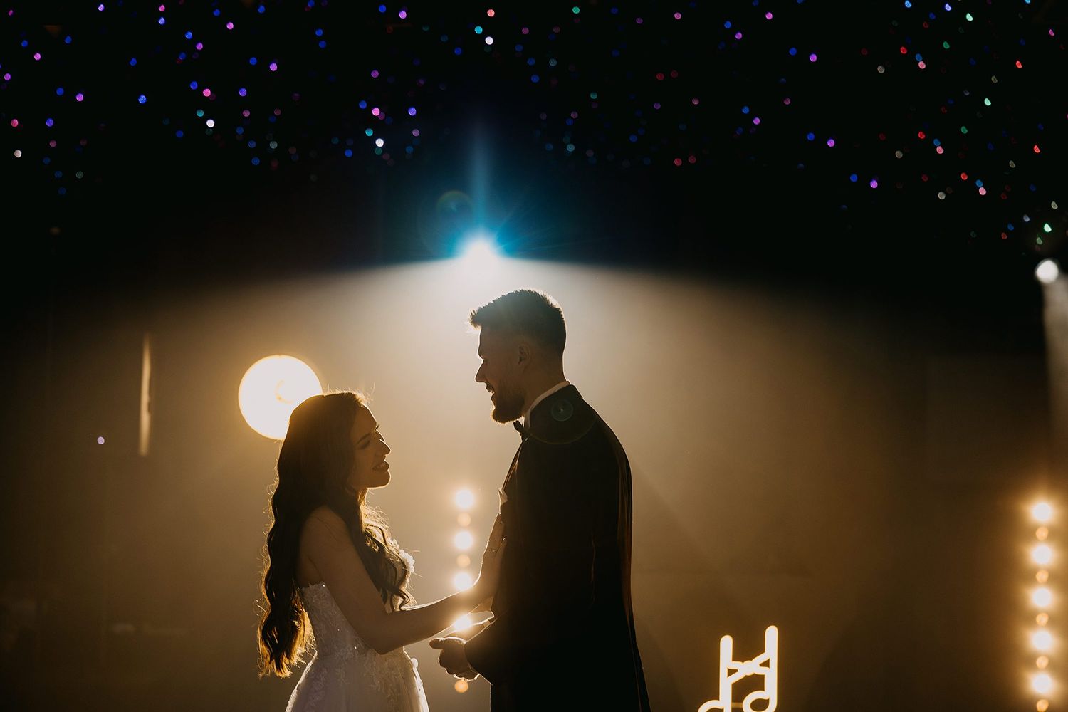 Romantic silhouette of bride and groom facing each other under a sparkling starlit ceiling at their wedding reception.