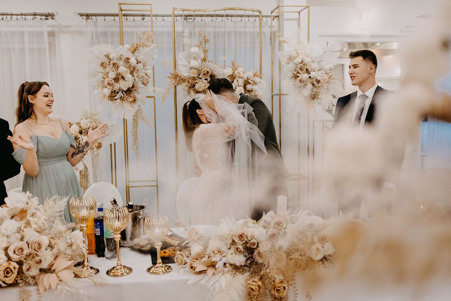 Bride and groom share a kiss at decorated wedding reception table with gold floral arrangements.