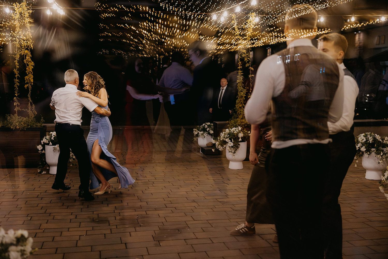 Couples dancing at a romantic wedding reception under twinkling fairy lights on a brick dance floor.