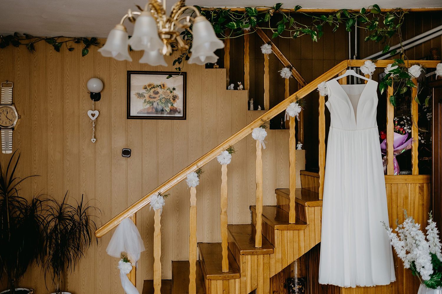White wedding dress hanging on staircase in warmly decorated wooden interior.