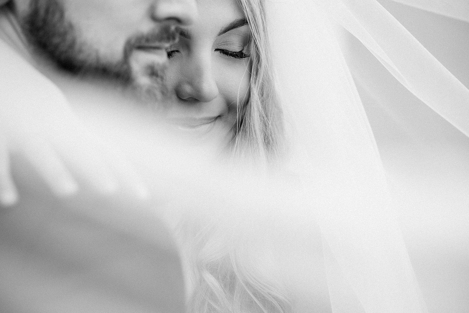 Intimate black and white portrait of bride smiling under wedding veil.