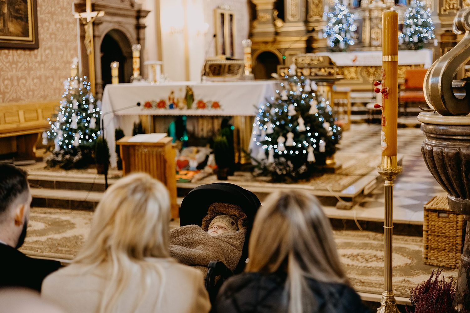 Family sits in a decorated Catholic church during a baby christening ceremony.