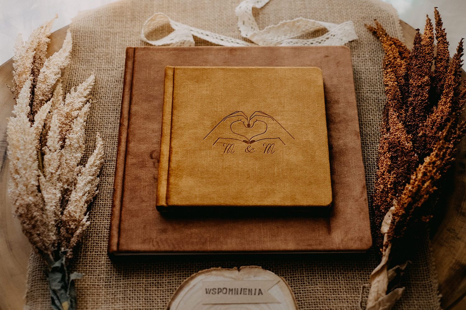 Tan velvet photo album with heart emblem on brown book, surrounded by dried grasses on burlap.