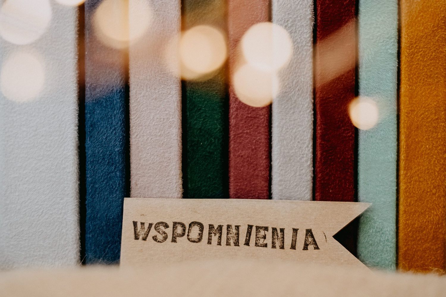 Wooden arrow-shaped Wspomnienia bookmark tag displayed against colorful fabric swatches in various colors.