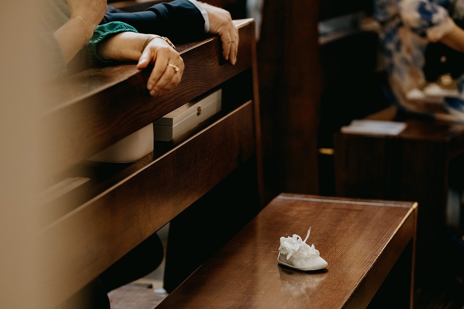 Tiny white baby shoe rests on wooden church pew during baptism ceremony.