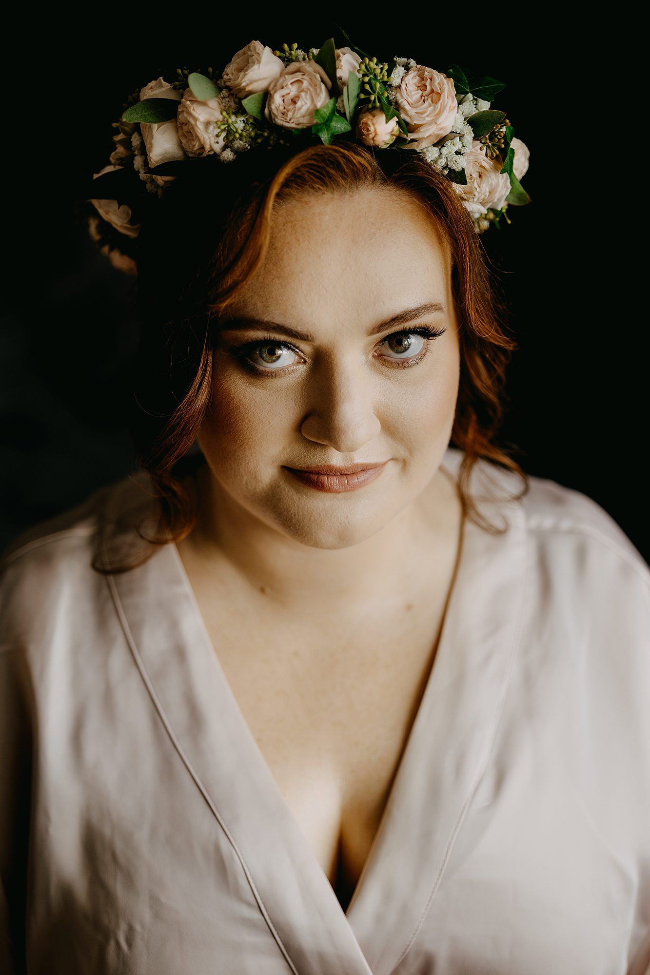 Bride wearing a floral crown of pink roses and greenery with soft makeup and a white wrap dress.