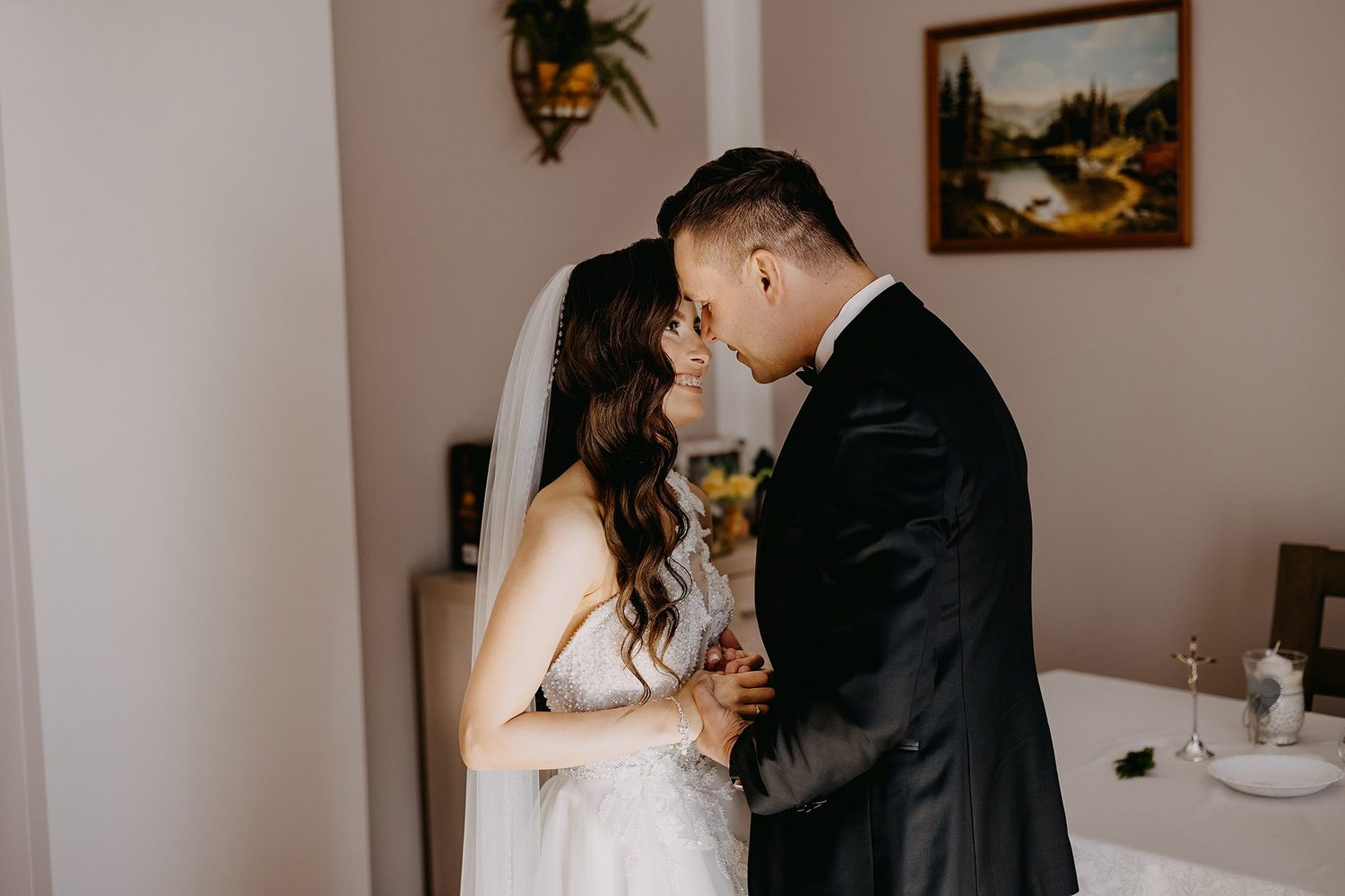 Bride in white veil and groom in black suit share intimate romantic moment before wedding ceremony.