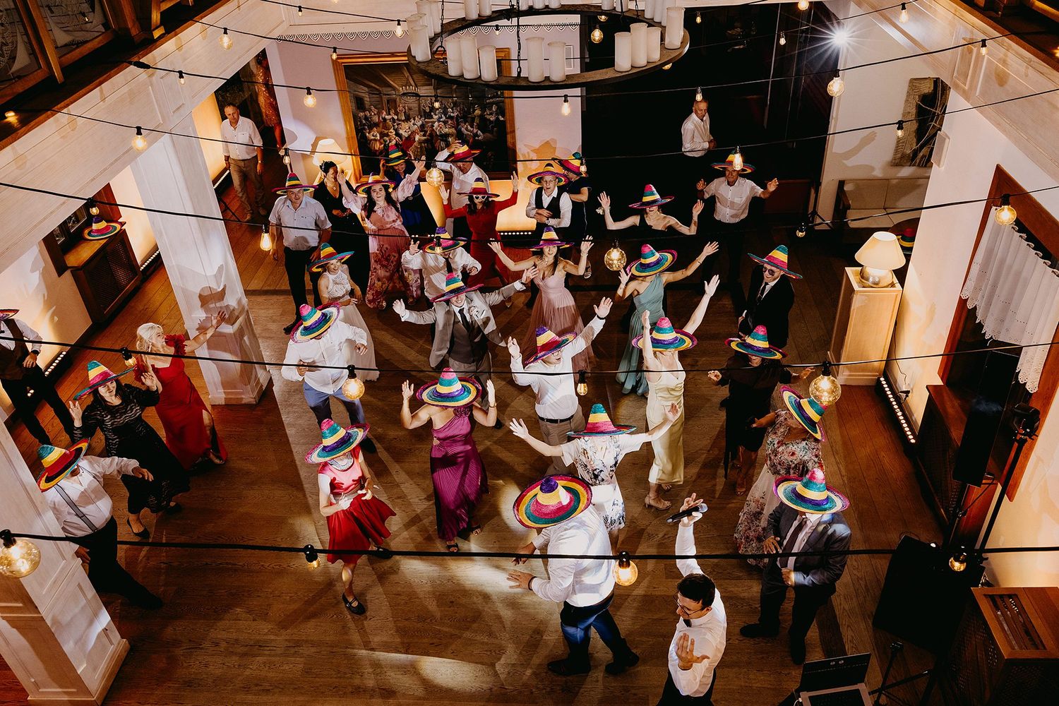 Aerial view of wedding guests in colorful folk costumes performing traditional circle dance on wooden floor.