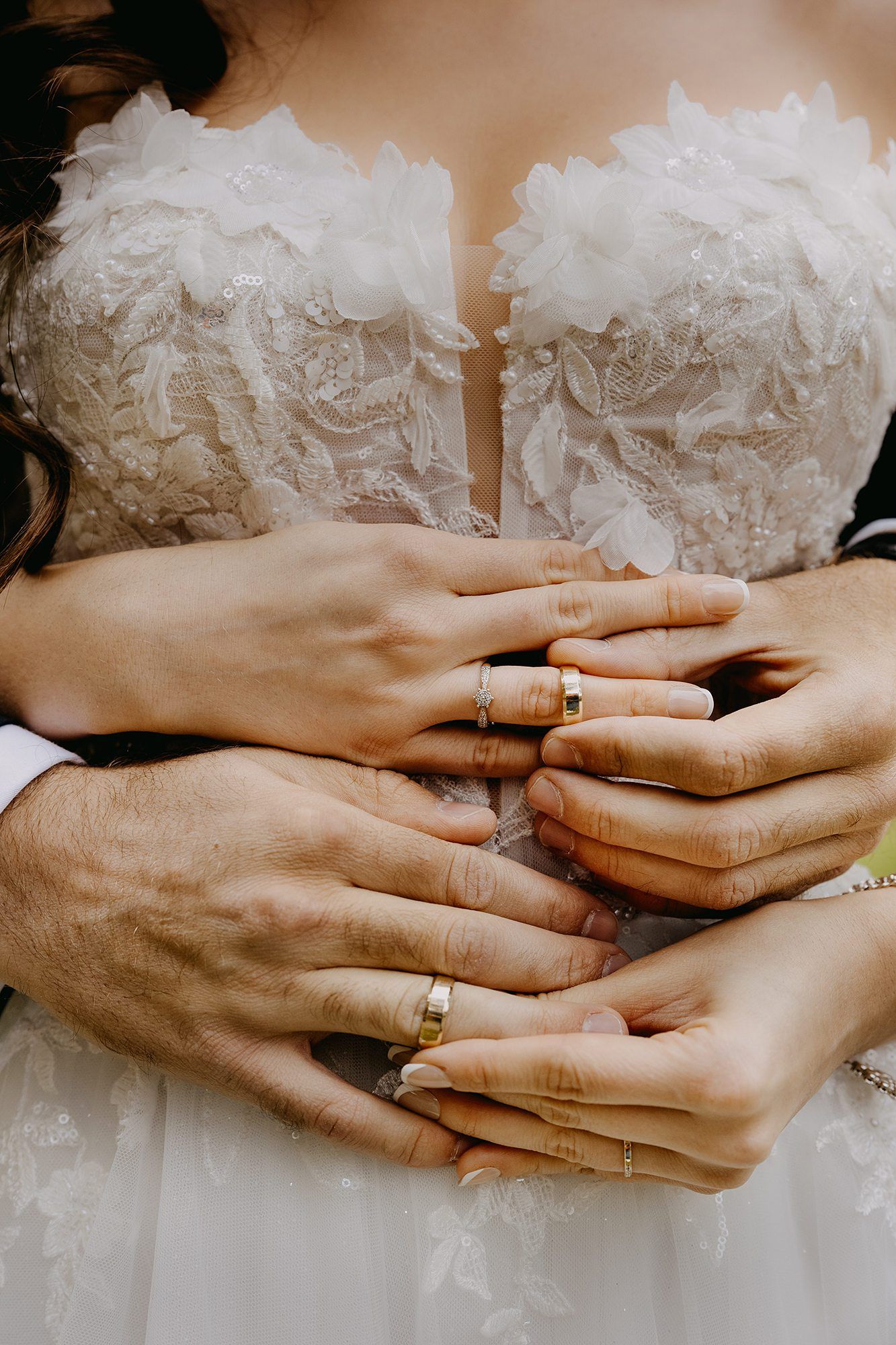 Close-up of bride and groom hands intertwined showing gold wedding rings against a lace bridal gown.