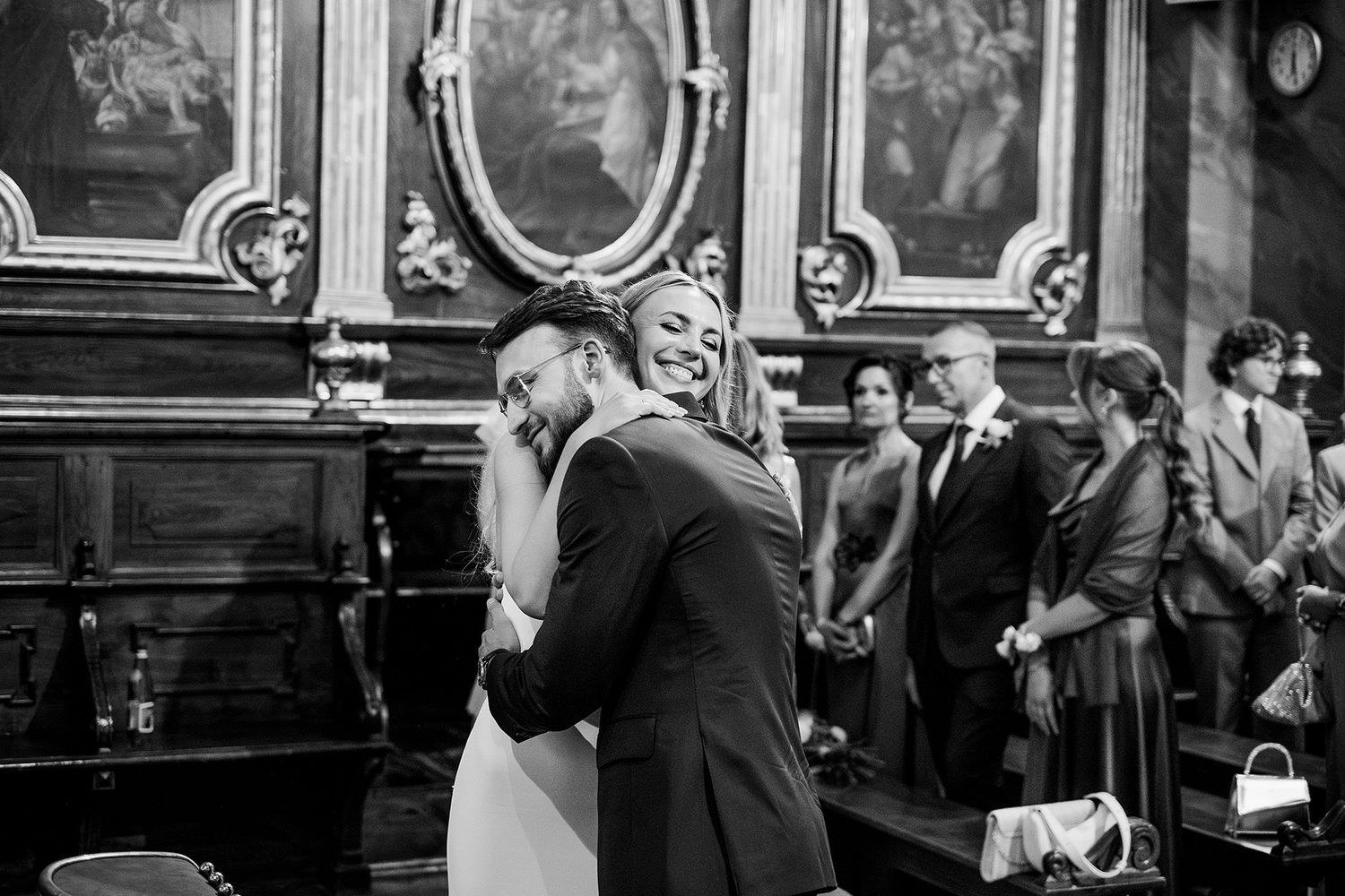 Black and white photo of a joyful couple embracing during their wedding ceremony in an elegant historic venue.