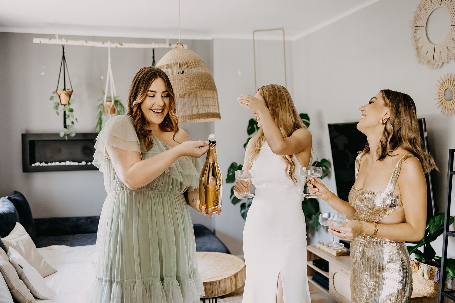 Three women celebrating with champagne during bridal party preparations at home.