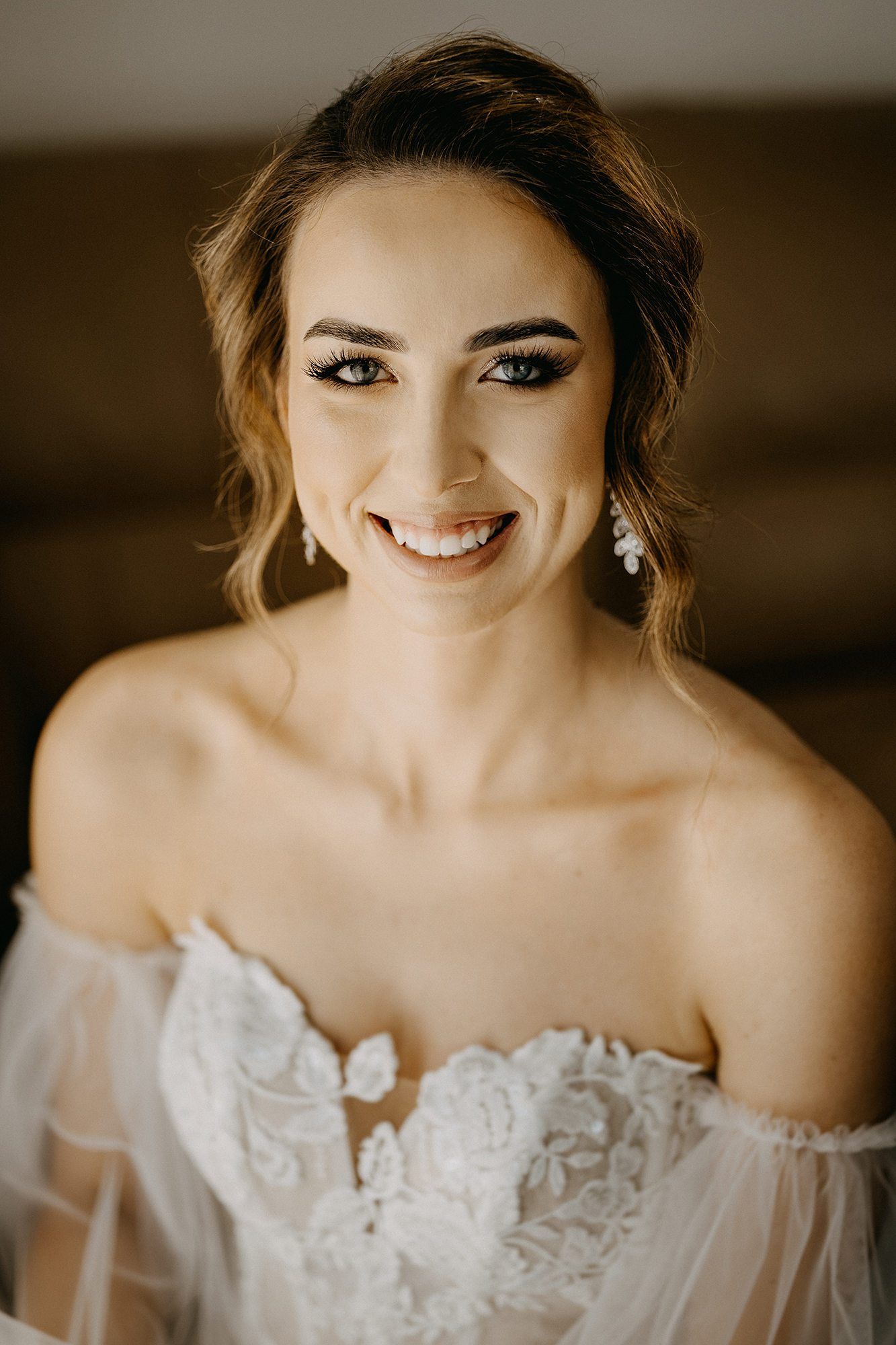 Beautiful smiling bride in off-shoulder lace wedding dress with elegant earrings.