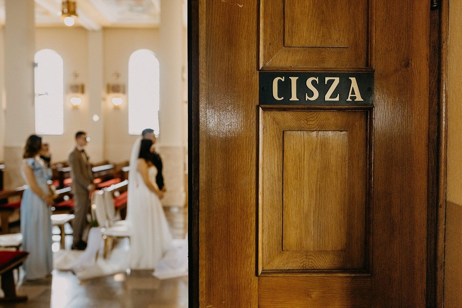 Wooden church door with a CISZA silence sign during a wedding ceremony with guests in background.