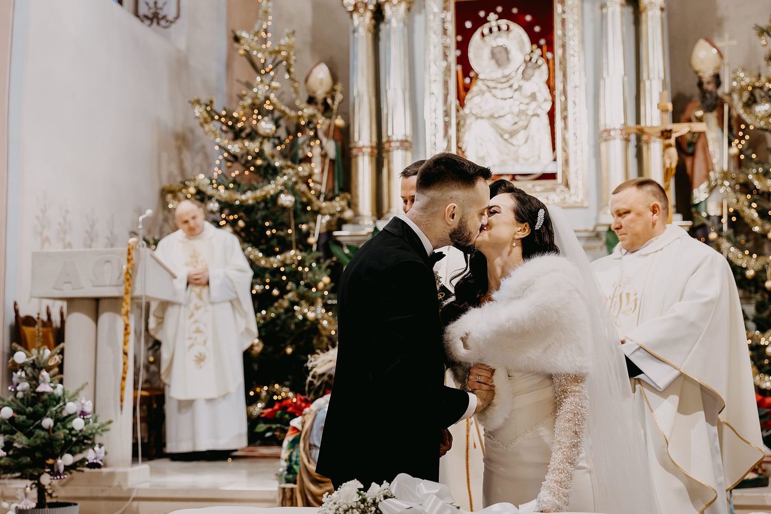 Bride and groom share a kiss at the altar of a beautifully decorated Christmas wedding ceremony.