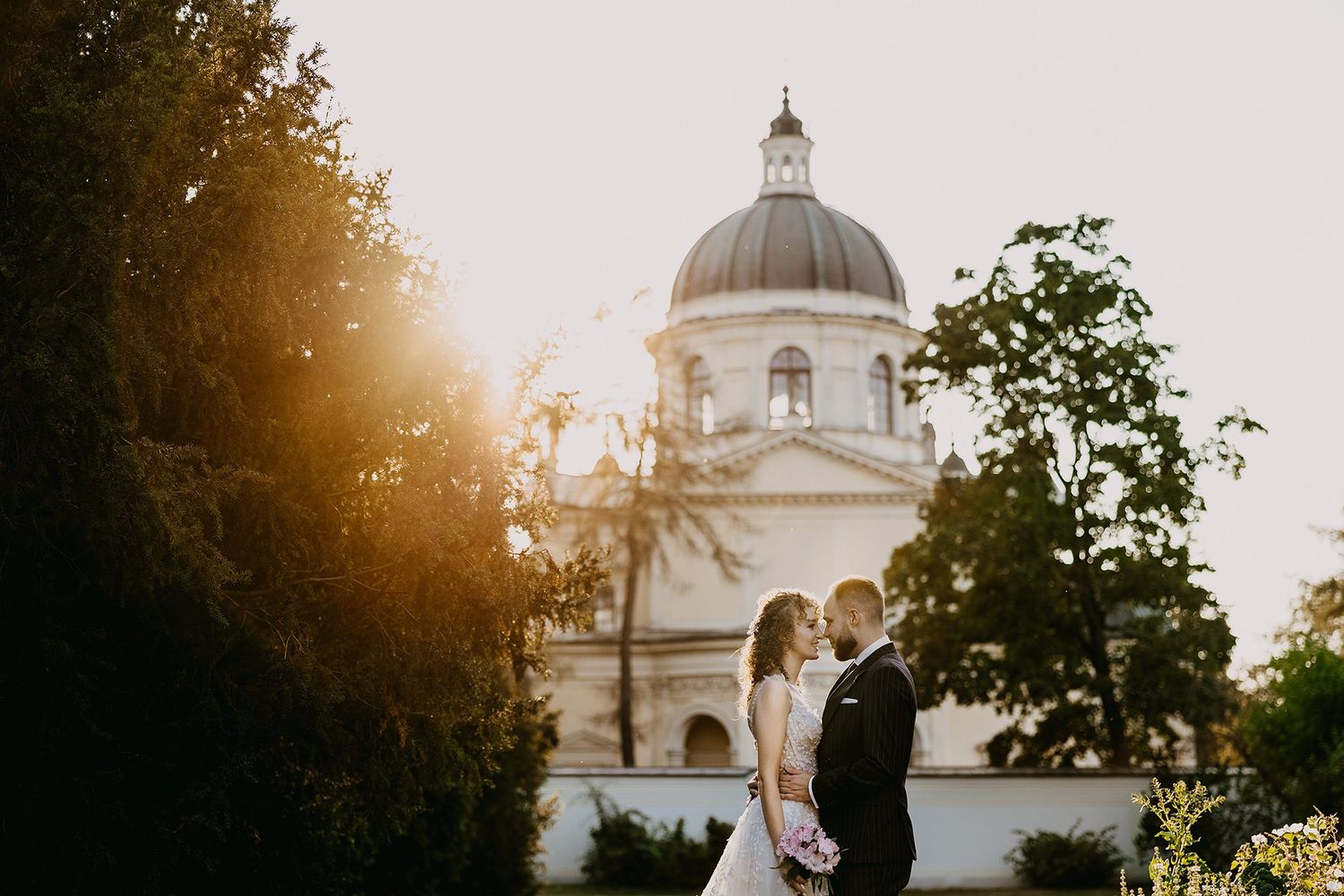Couple standing close together with a stunning domed church glowing in golden sunlight.