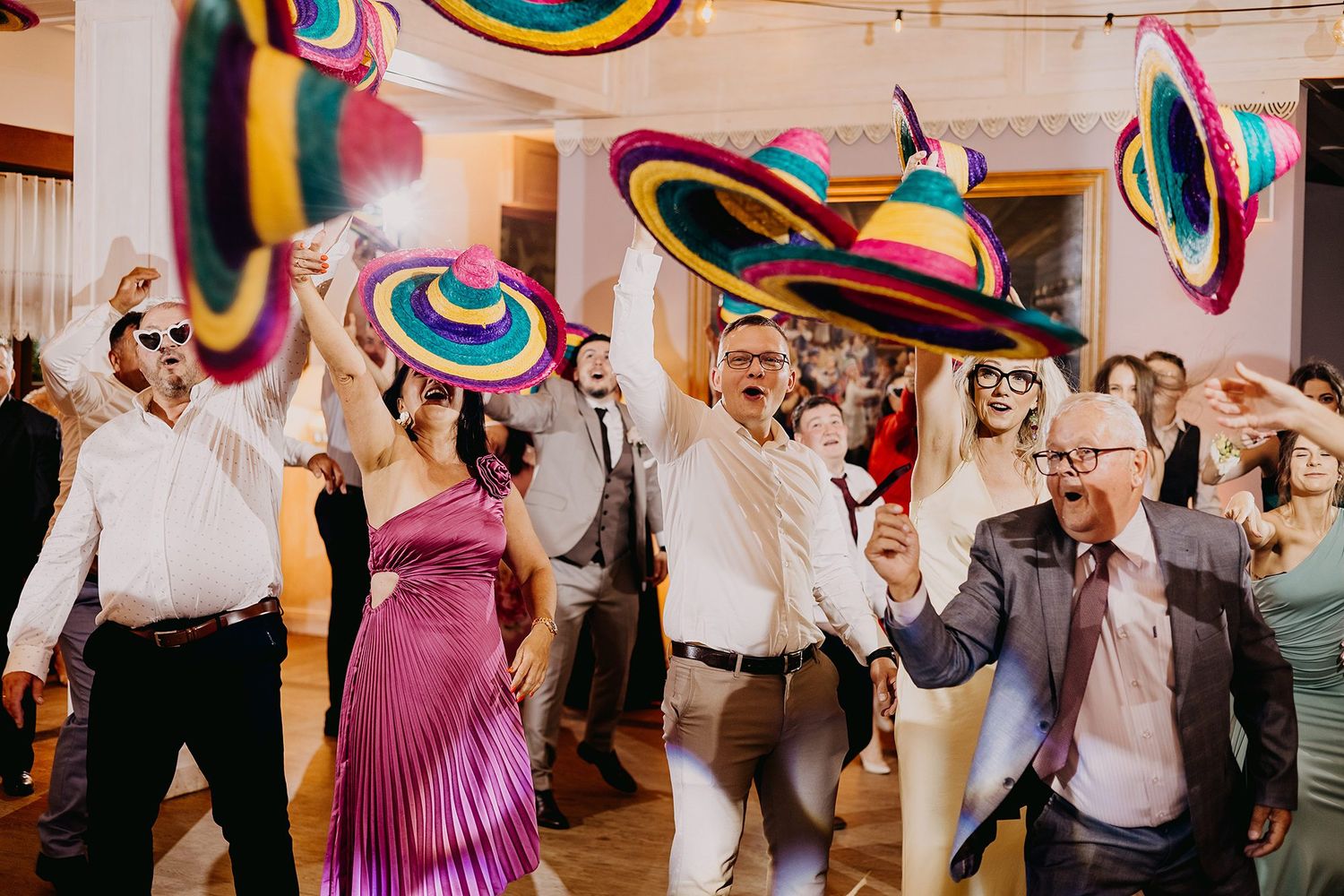 Guests dancing and celebrating at a lively wedding reception while waving colorful sombrero hats in the air.