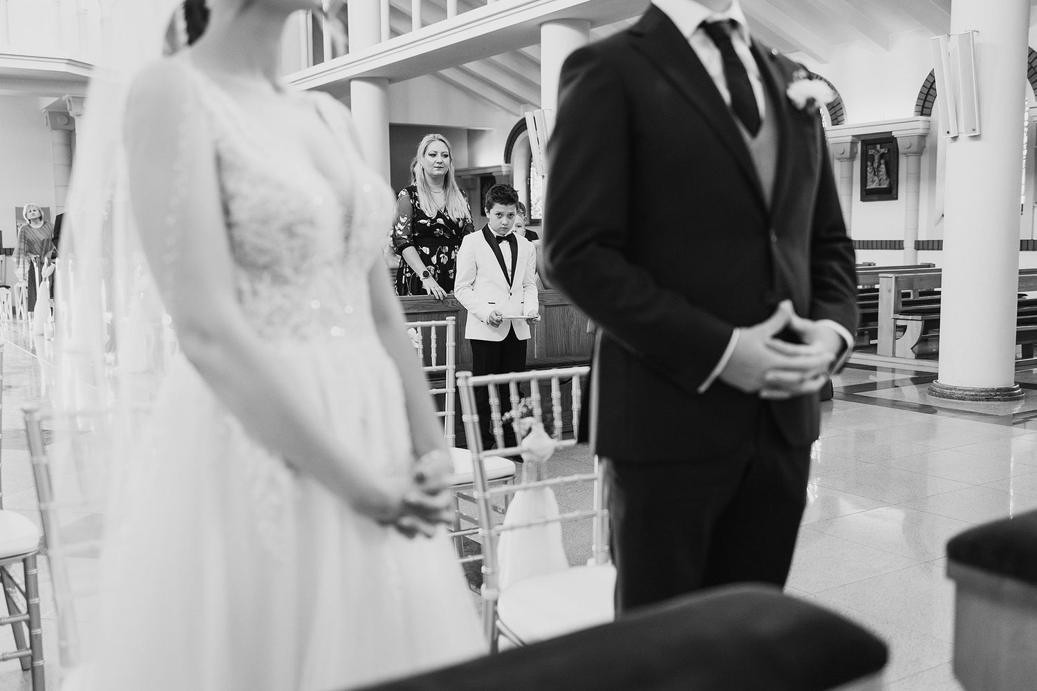 Black and white photo of bride and groom holding hands at wedding ceremony altar.