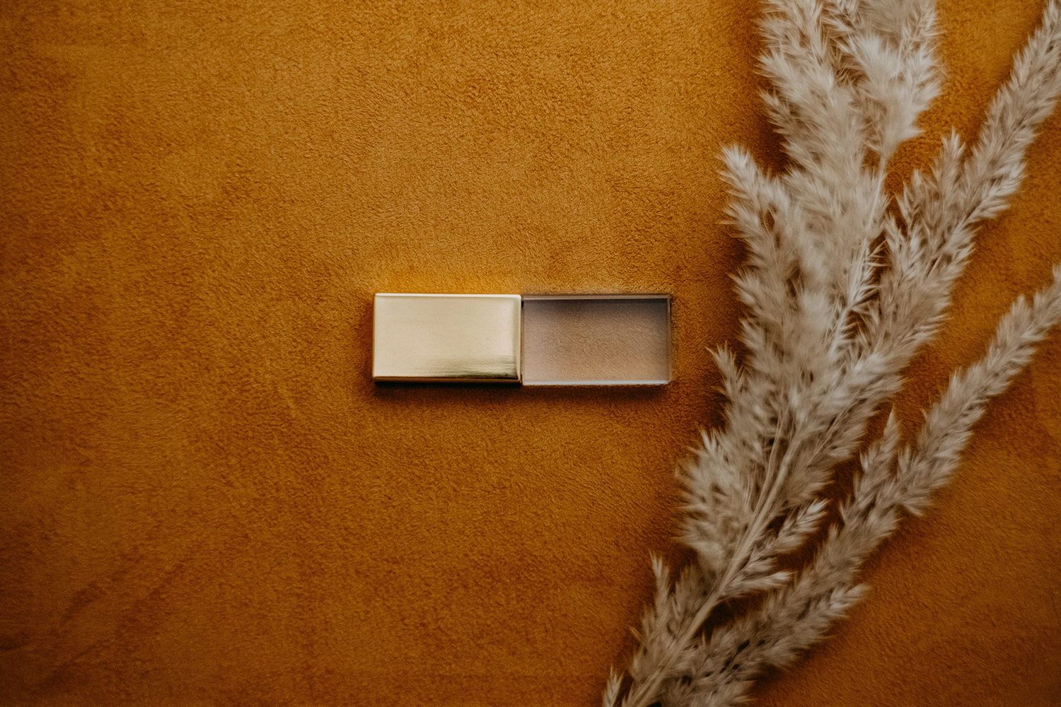 Sleek metallic USB flash drive on golden textured surface with dried pampas grass decoration.