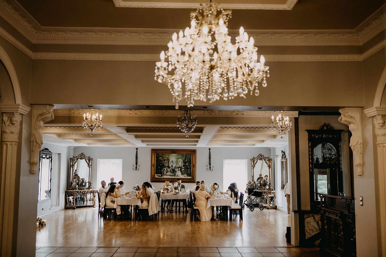 Elegant banquet hall with grand crystal chandelier, ornate decor, and guests seated at tables for a formal event.