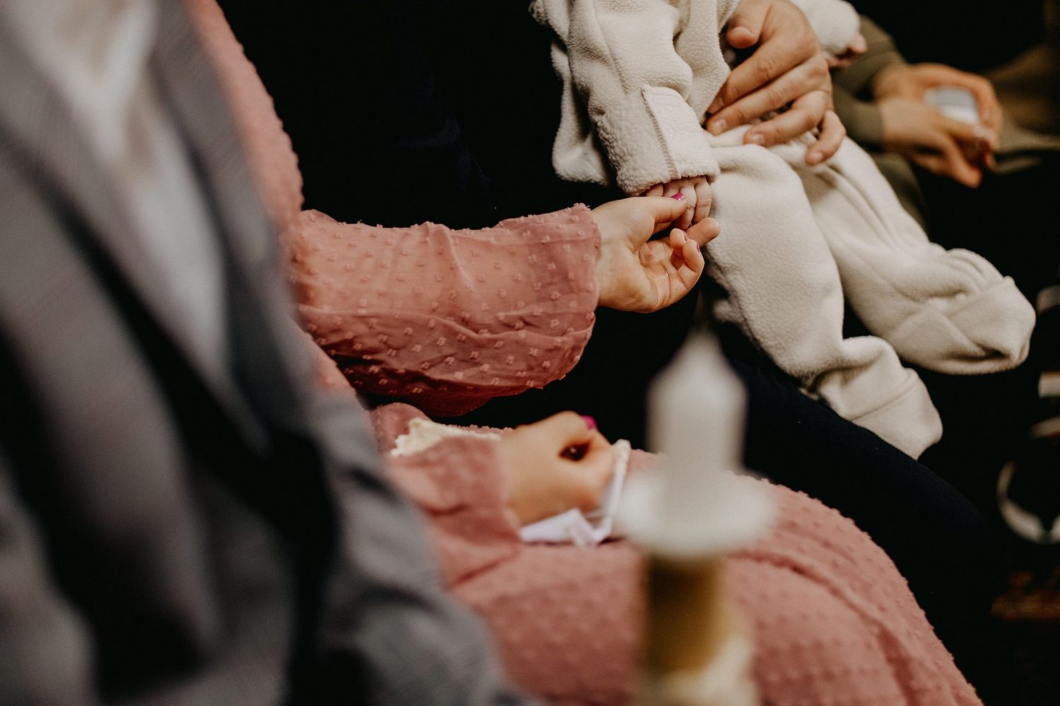 An adult gently holds a baby's tiny feet near a lit candle during a baptism ceremony.