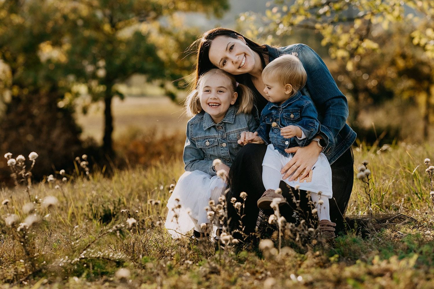 Mother hugging two young children in autumn wildflower meadow.