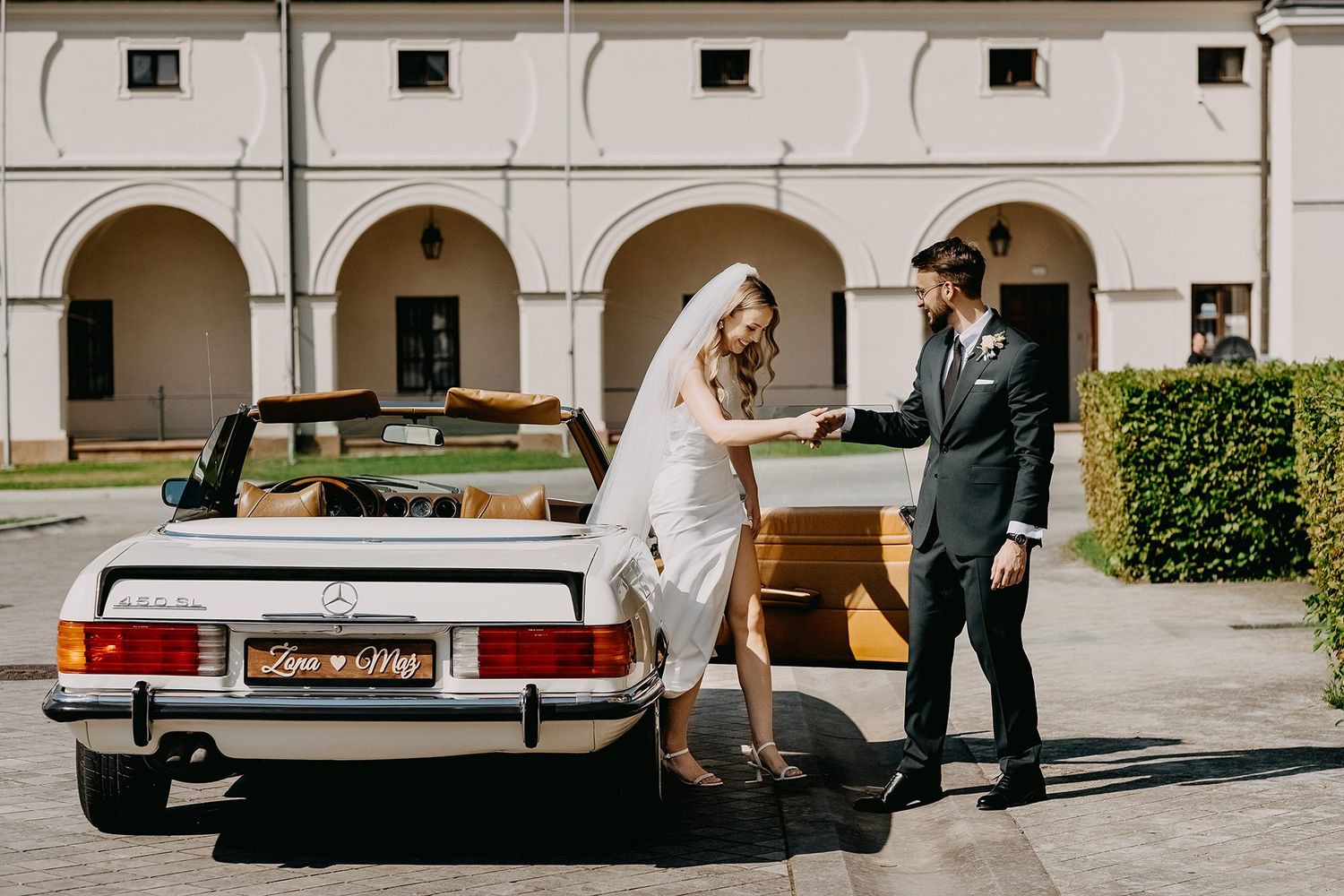 Bride and groom posing beside vintage white Mercedes convertible wedding car.