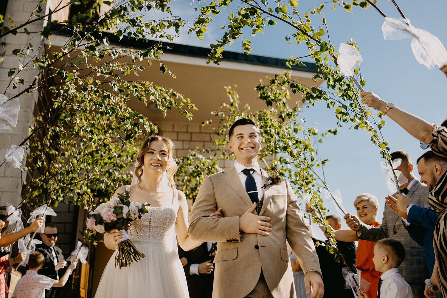 Smiling newlyweds walk through confetti shower outside a church on their sunny wedding day.