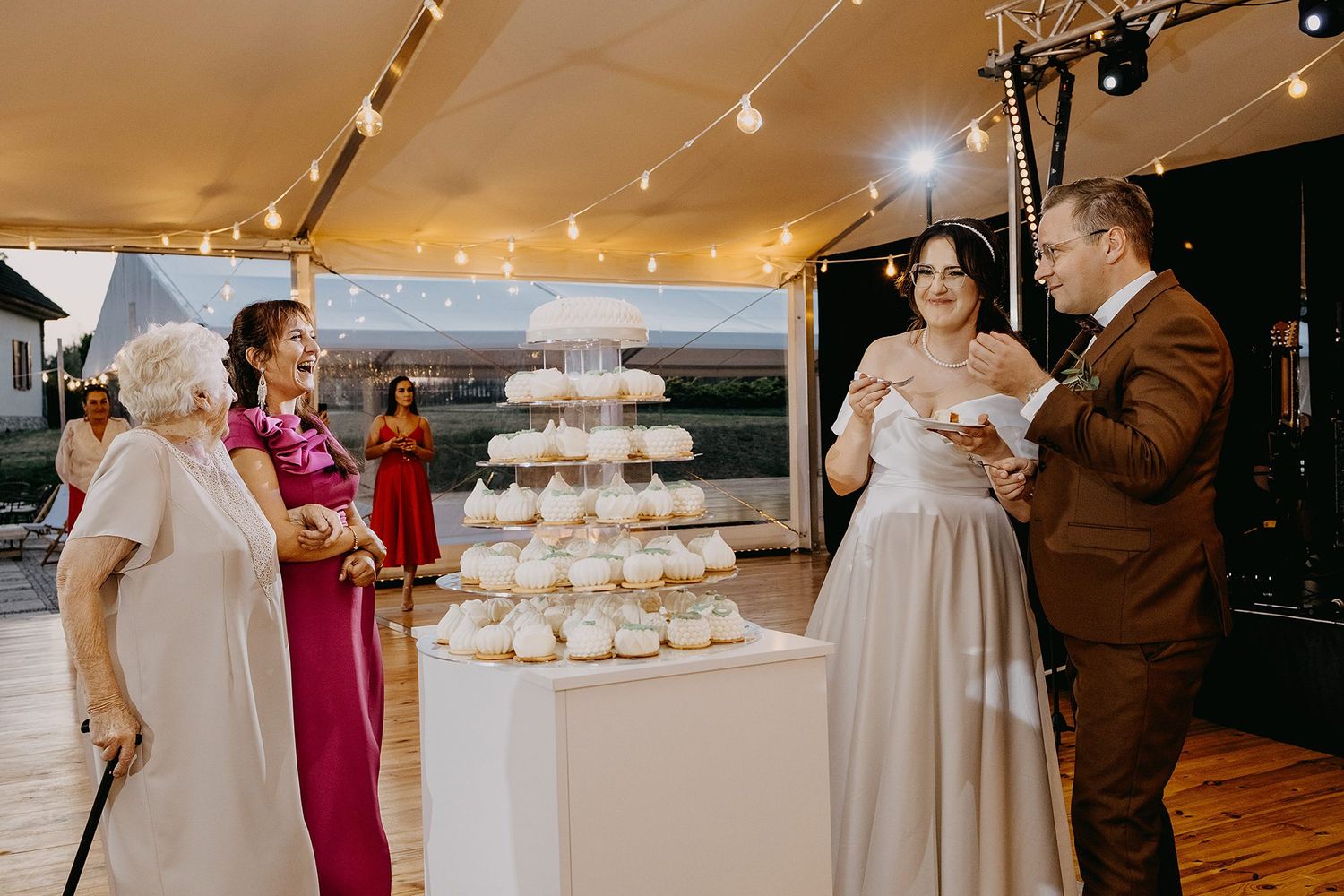 Bride and groom cutting wedding cake at elegant reception with string lights.