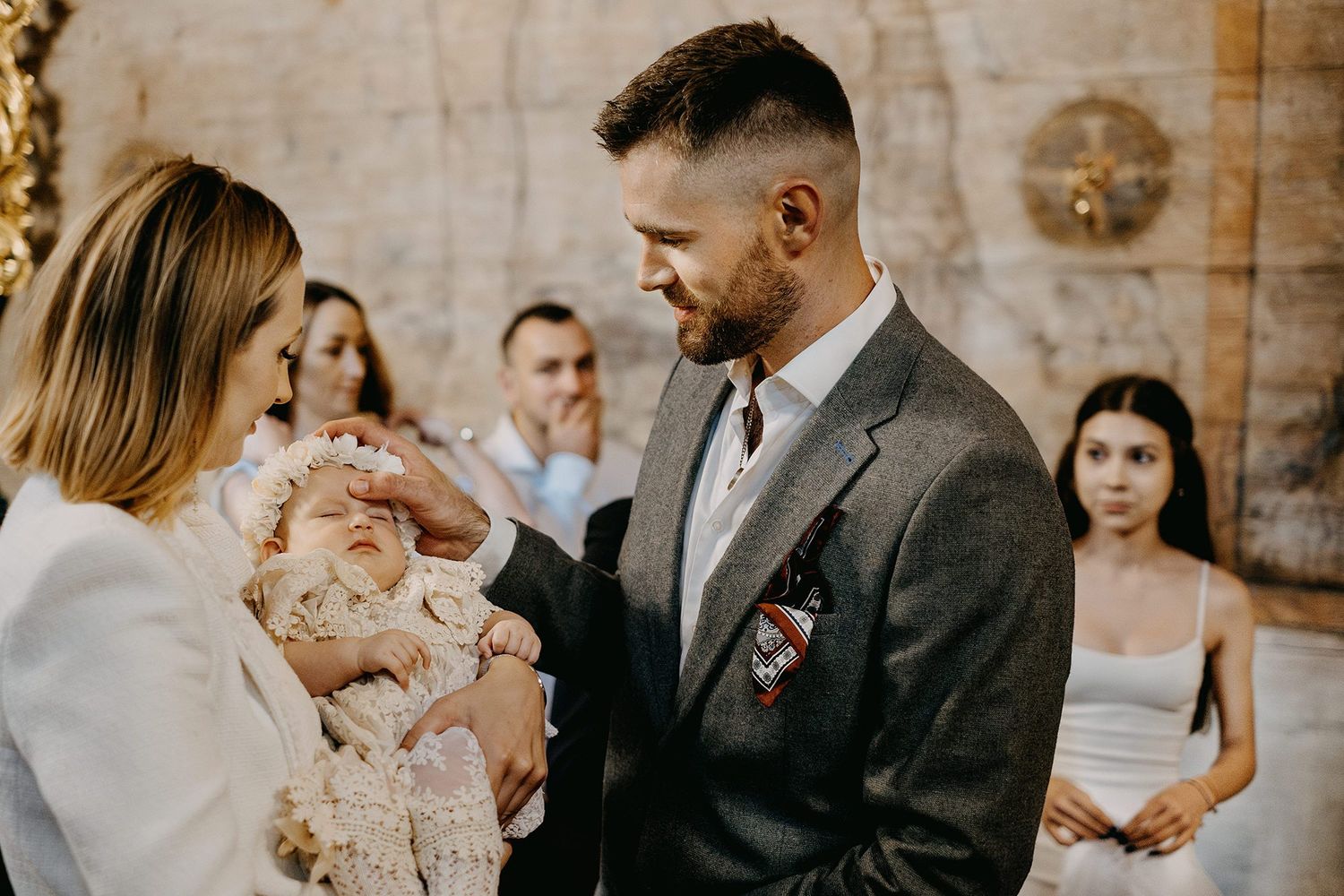 Father touching baptized baby held by mother during christening ceremony in decorated church.