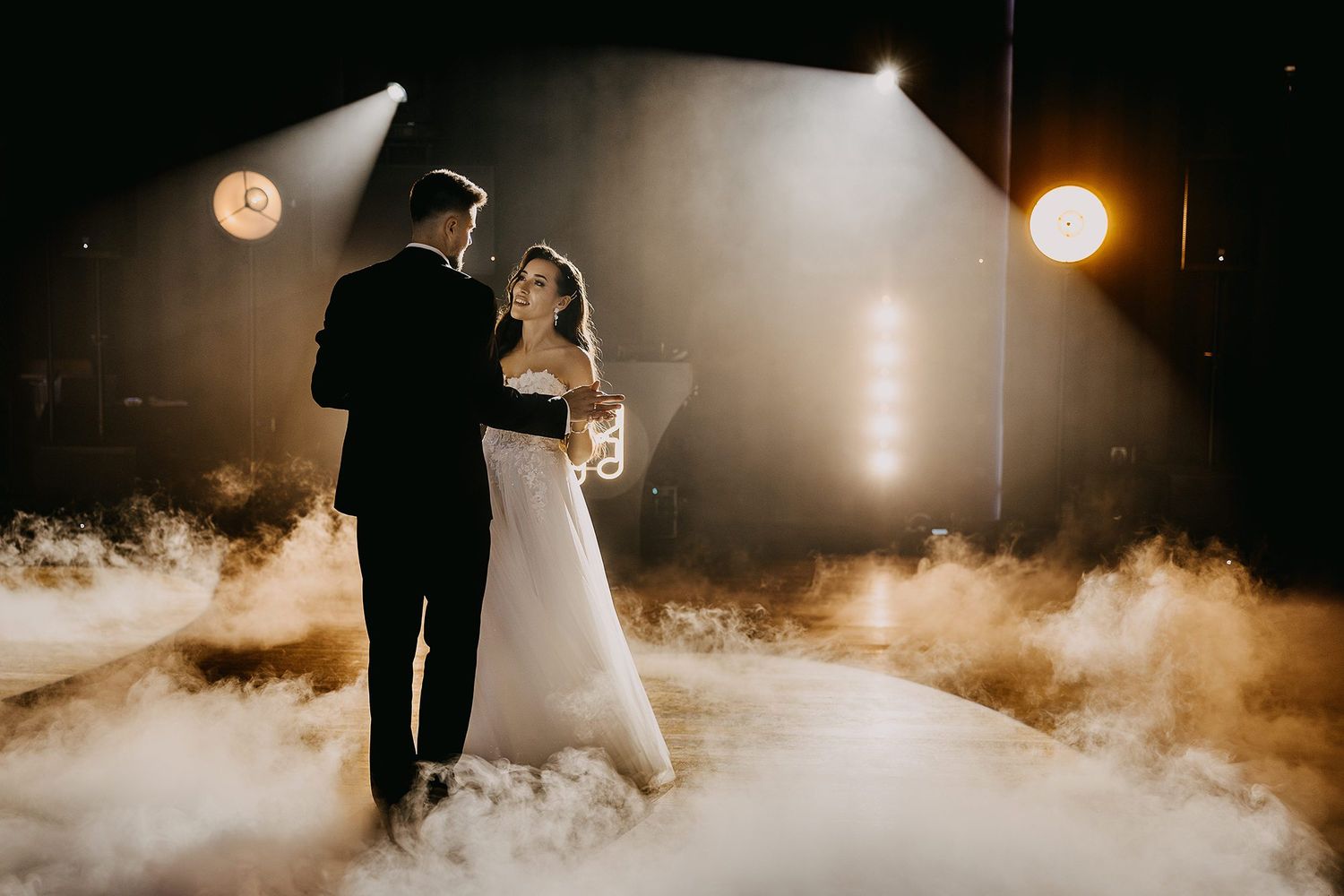 A bride and groom share their first dance surrounded by dramatic fog and stage lighting at their reception.