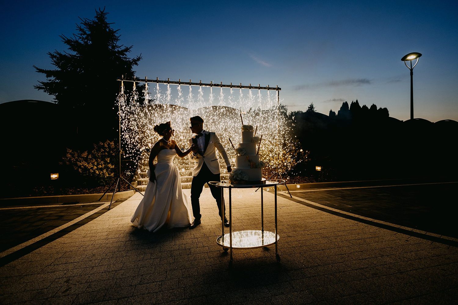 Bride and groom dance in silhouette against sparkling light display at twilight wedding celebration.