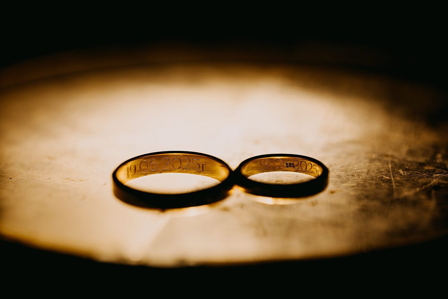 Two gold wedding bands resting together on a textured surface in warm golden light.