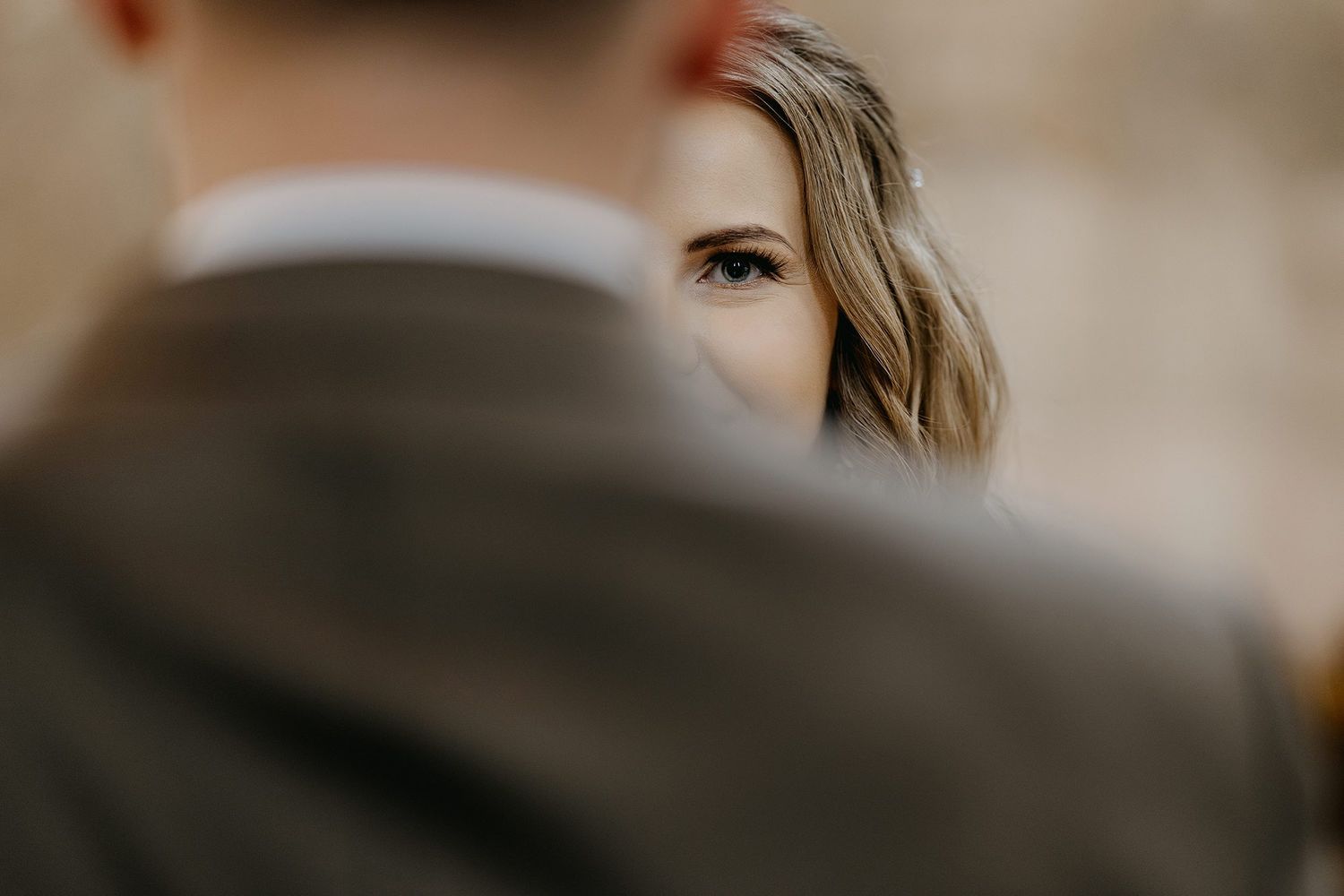 Bride gazes over grooms shoulder in a romantic close-up wedding portrait with soft bokeh background.