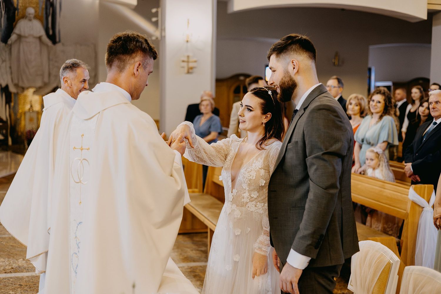 Bride smiling as priest blesses her hand during Catholic wedding ceremony at church altar.