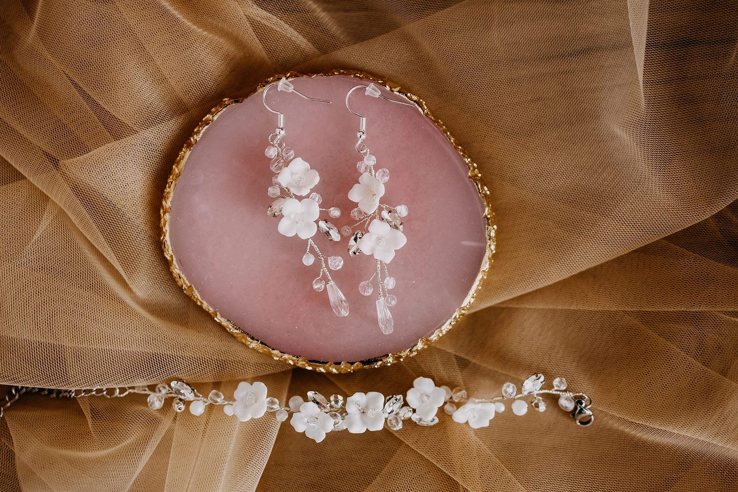 Elegant bridal hair vine with white flowers and pearls displayed on a pink agate slice with gold tulle.