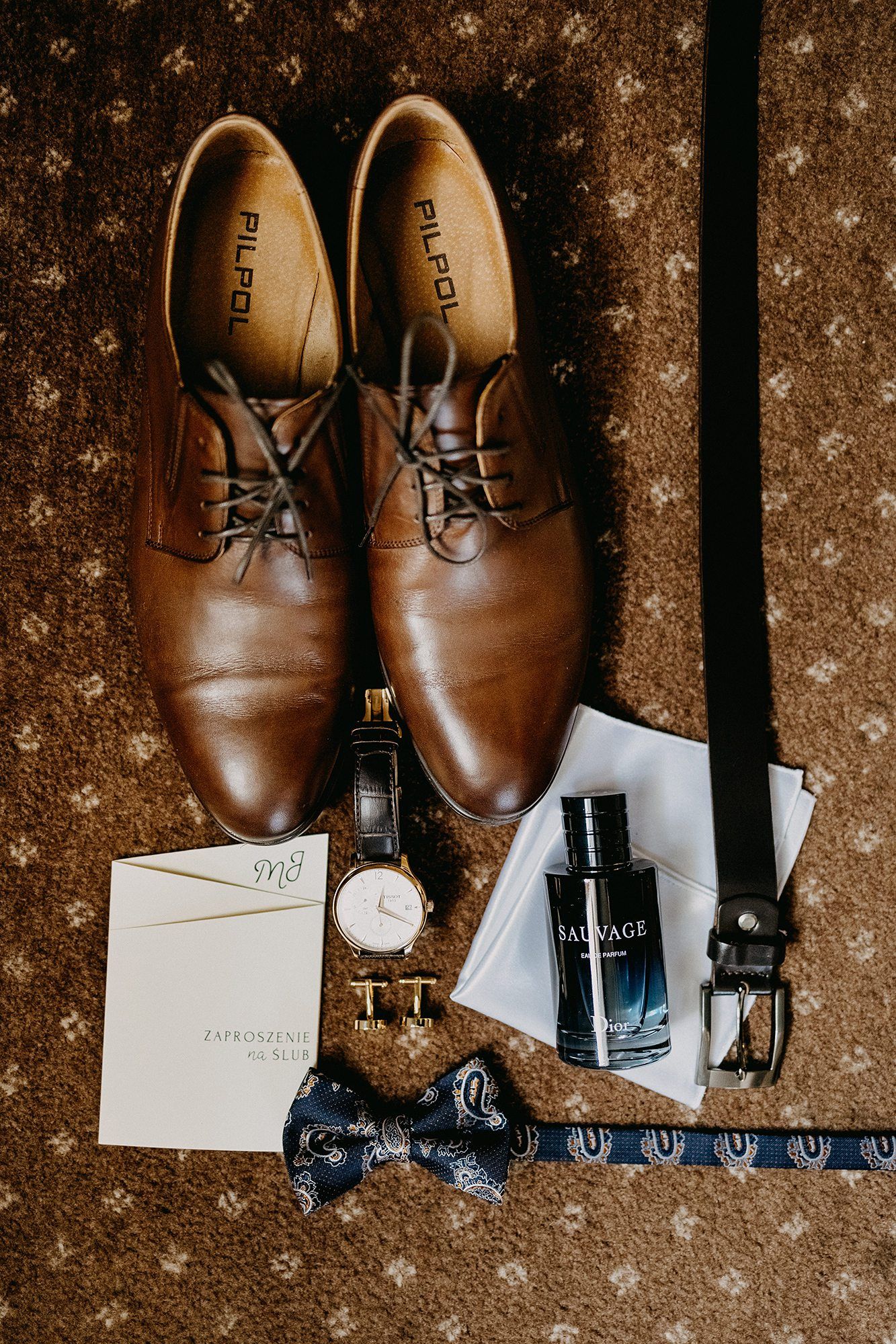 Groom wedding flat lay featuring brown leather Oxford shoes, Sauvage cologne, watch, cufflinks, and bow tie.