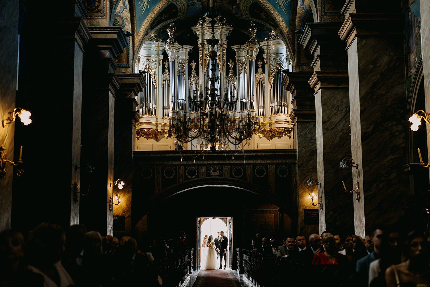 Couple exchanges vows in a stunning historic church with grand pipe organ and chandelier.