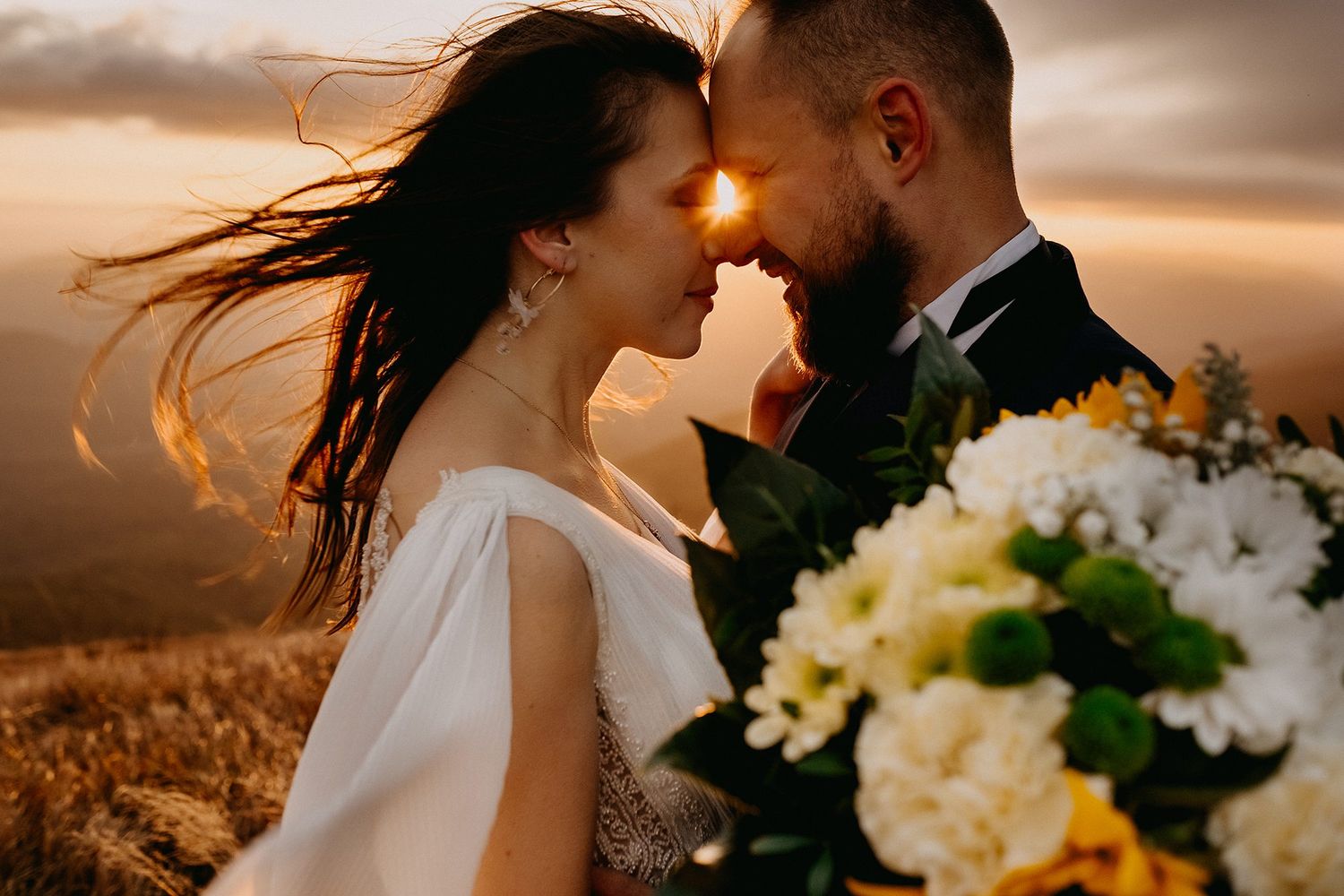 A bride and groom touch foreheads romantically at sunset, bride holding a white hydrangea bouquet.
