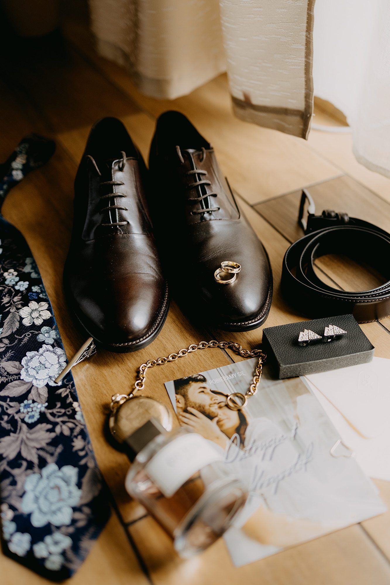Groom wedding details flat lay with brown Oxford shoes, floral tie, gold watch chain, and cufflinks.