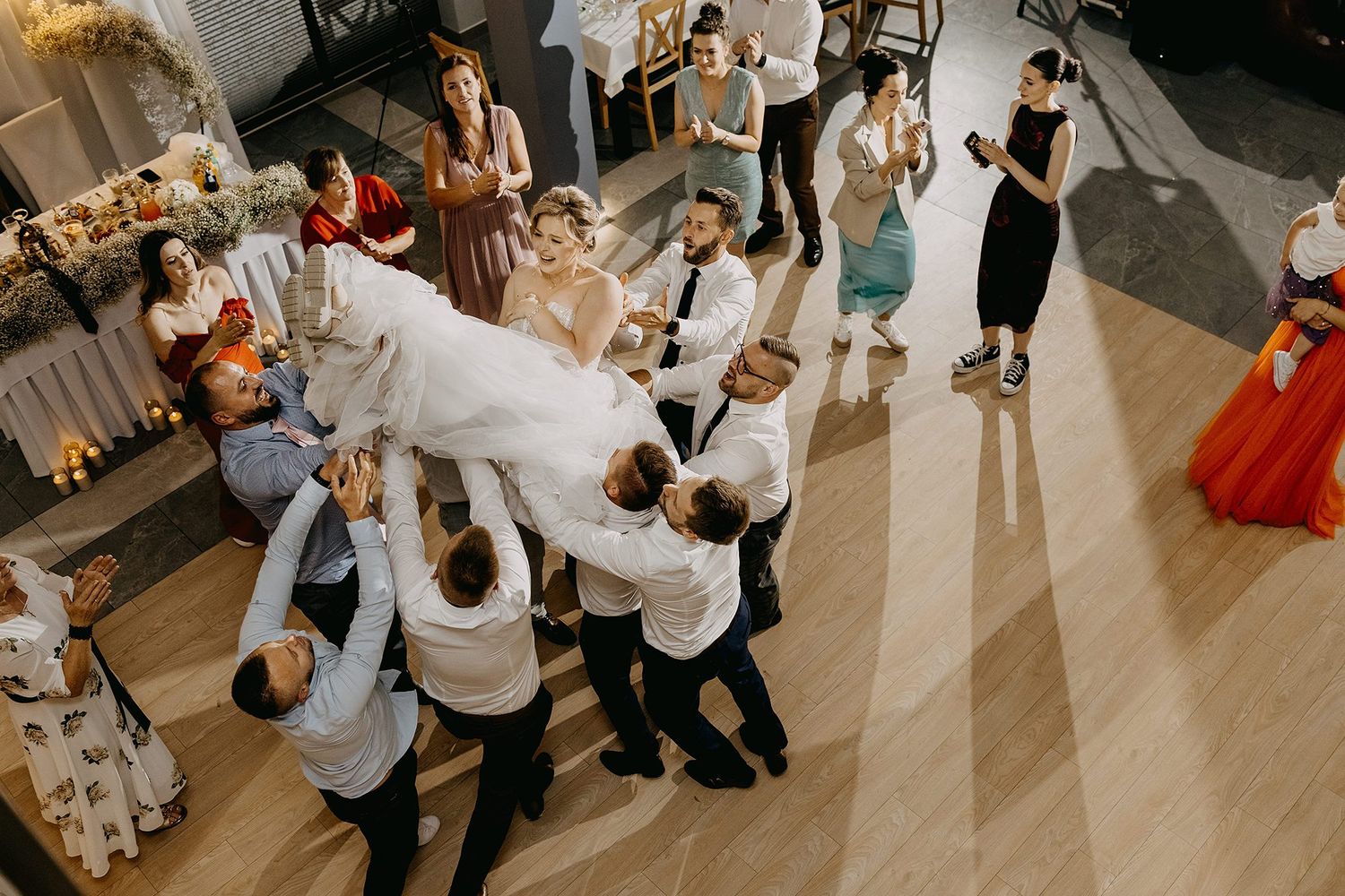 Groomsmen joyfully lifting the bride in the air during a fun wedding reception celebration on the dance floor.