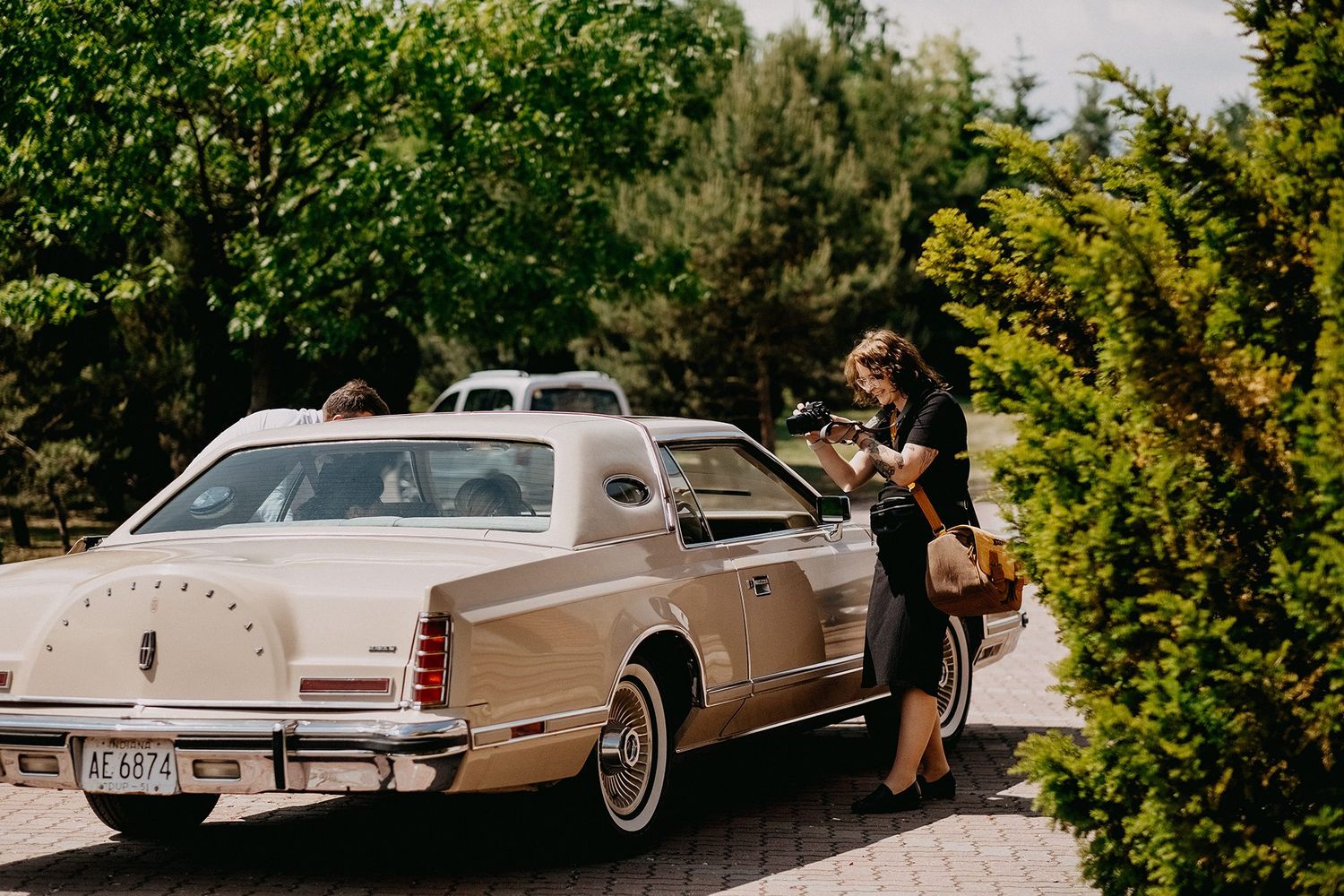 Female photographer reviewing shots on camera beside a classic beige Lincoln Continental luxury car.