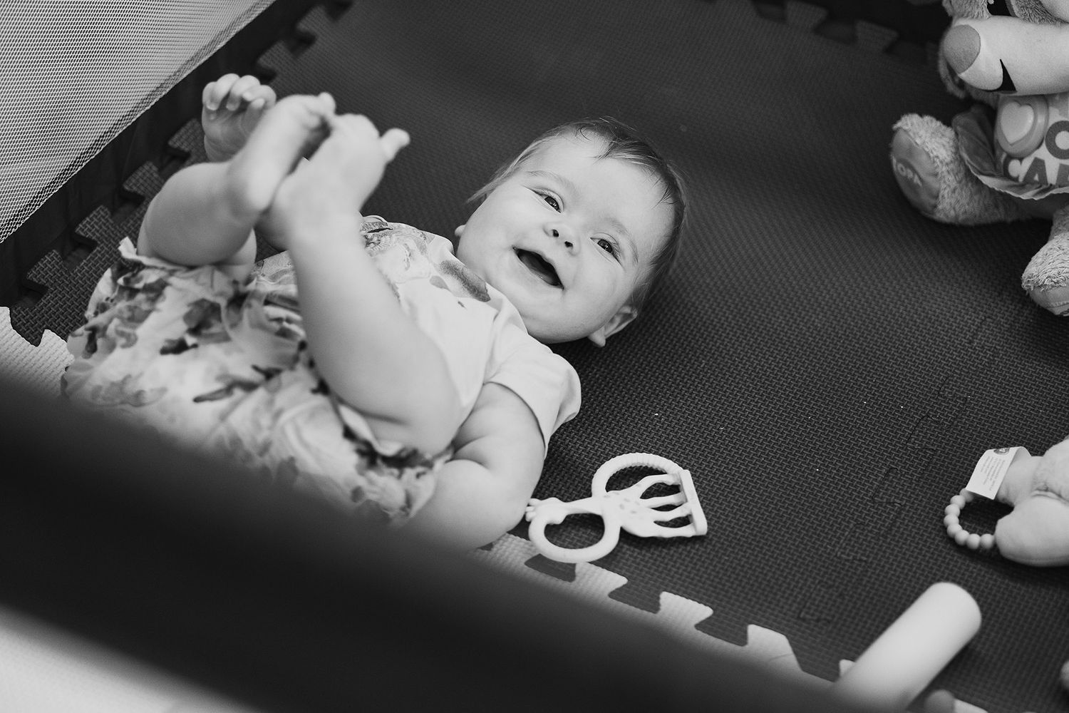 Laughing baby lying on back on a play mat in black and white photo.