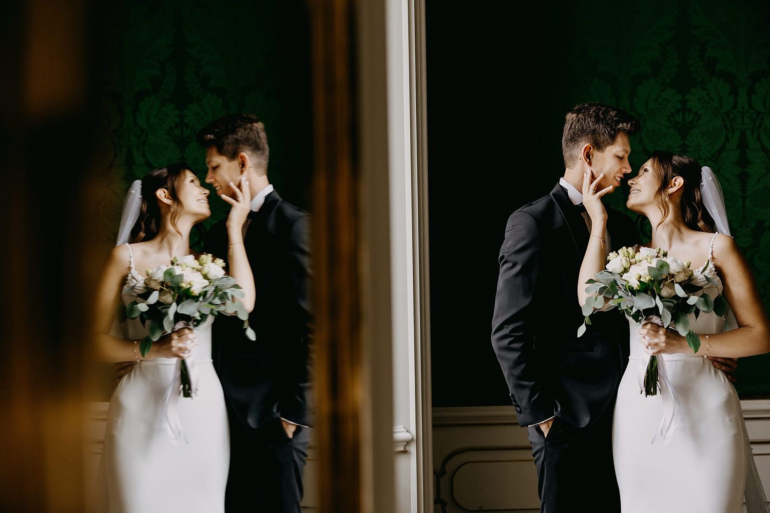 Wedding couple nearly kissing reflected in mirror, bride holding white bouquet in elegant room.