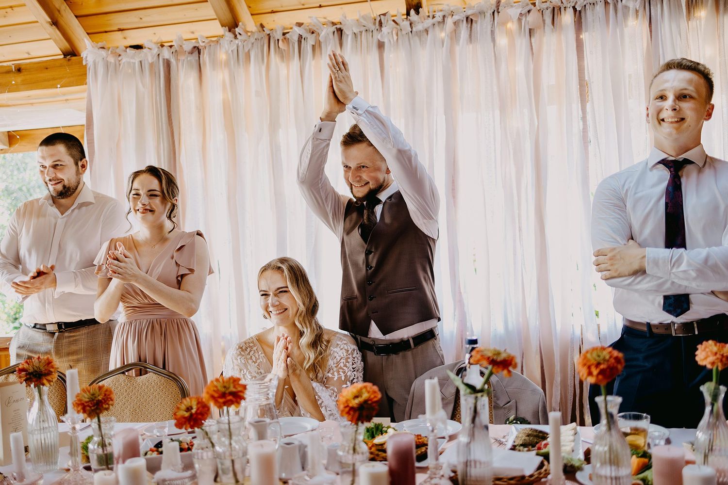 Wedding guests laughing and celebrating during a toast at an elegant reception with floral centerpieces.