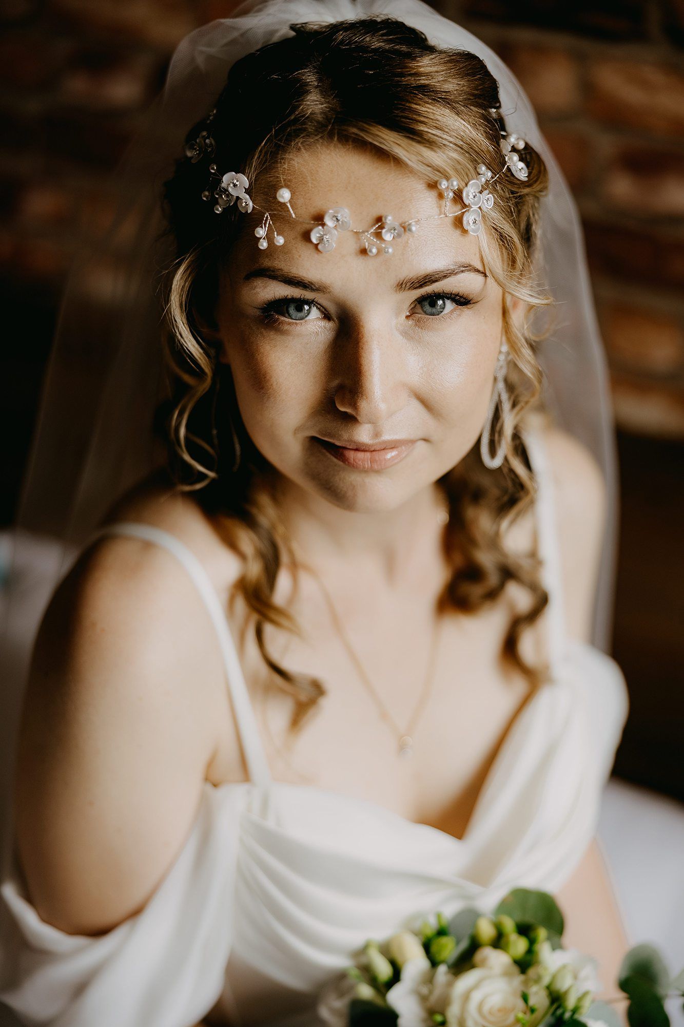 Portrait of bride with floral hair vine and veil holding white bouquet.