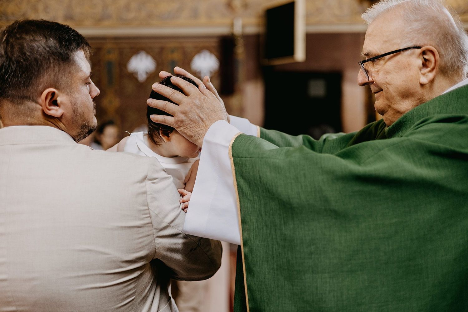 Catholic priest in green vestments placing hands on mans head during religious blessing ceremony.