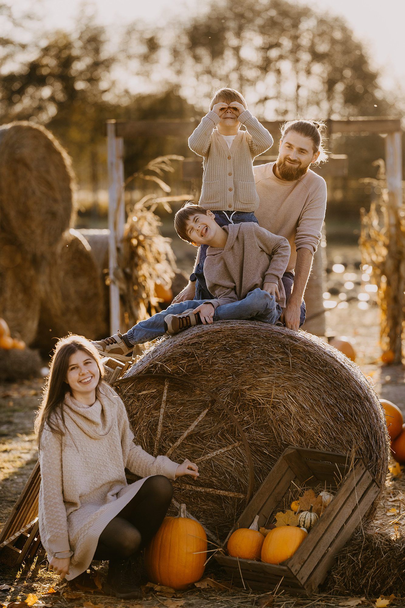 Family with two boys posing on a hay bale with pumpkins at a sunny autumn farm.