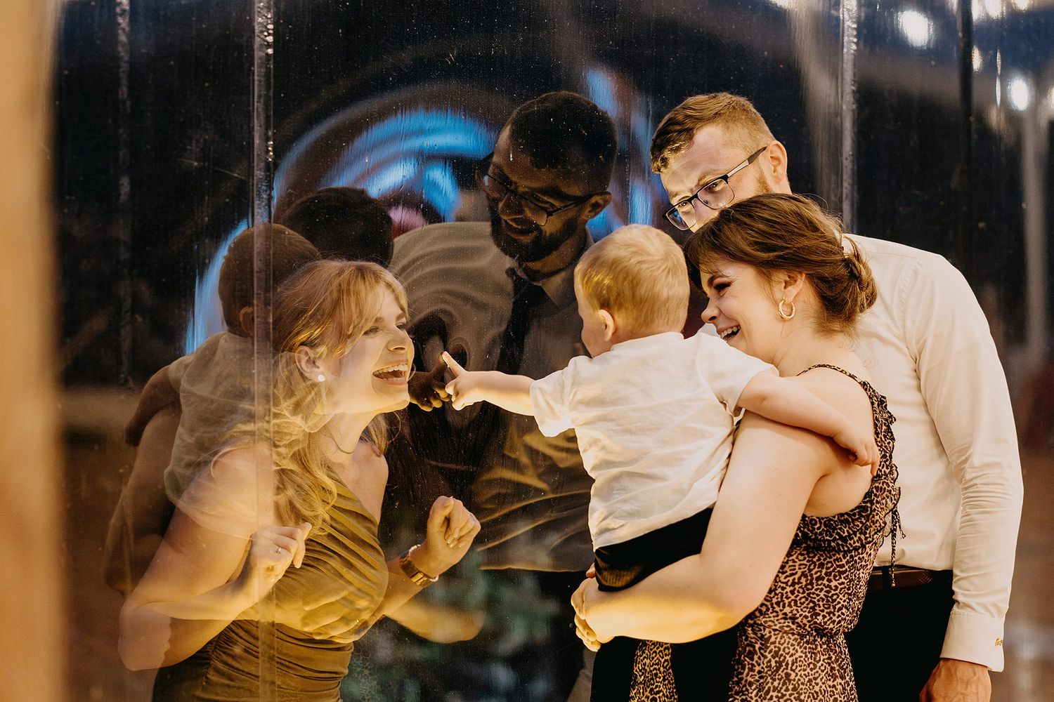 Wedding guests joyfully interacting with a baby during evening reception celebration indoors.